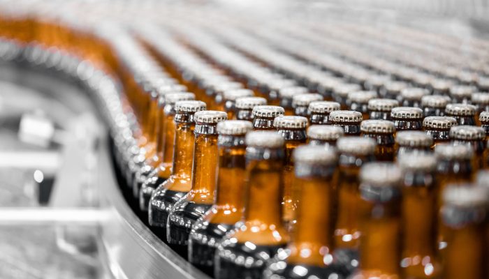 Glass bottles of beer on dark background with sun light. Concept brewery plant production line.
